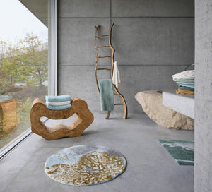 A&H Dune Bath Rug (round, foreground). A&H Lodge Towels in 235 Ice and 103 Ivory (on wood sculpture). Bay Bath Rug in 235 Ice (wood ladder). Legend Face Towels in Colour 299 on the countertop.