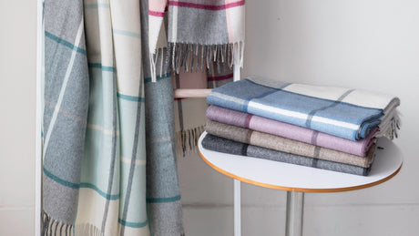 Mika Alpaca throws in Cyan (hanging, left) and Peony (hanging, right). The very bottom throw folded on the table is Onyx. The other folded throws are discontinued colours.